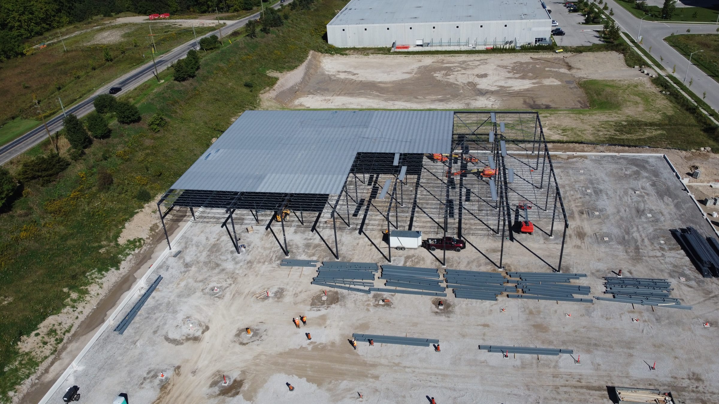 An aerial view of the steel frame from the other side: decked bays at the top, open frame bays below and steel members laid out in rows on the slab.