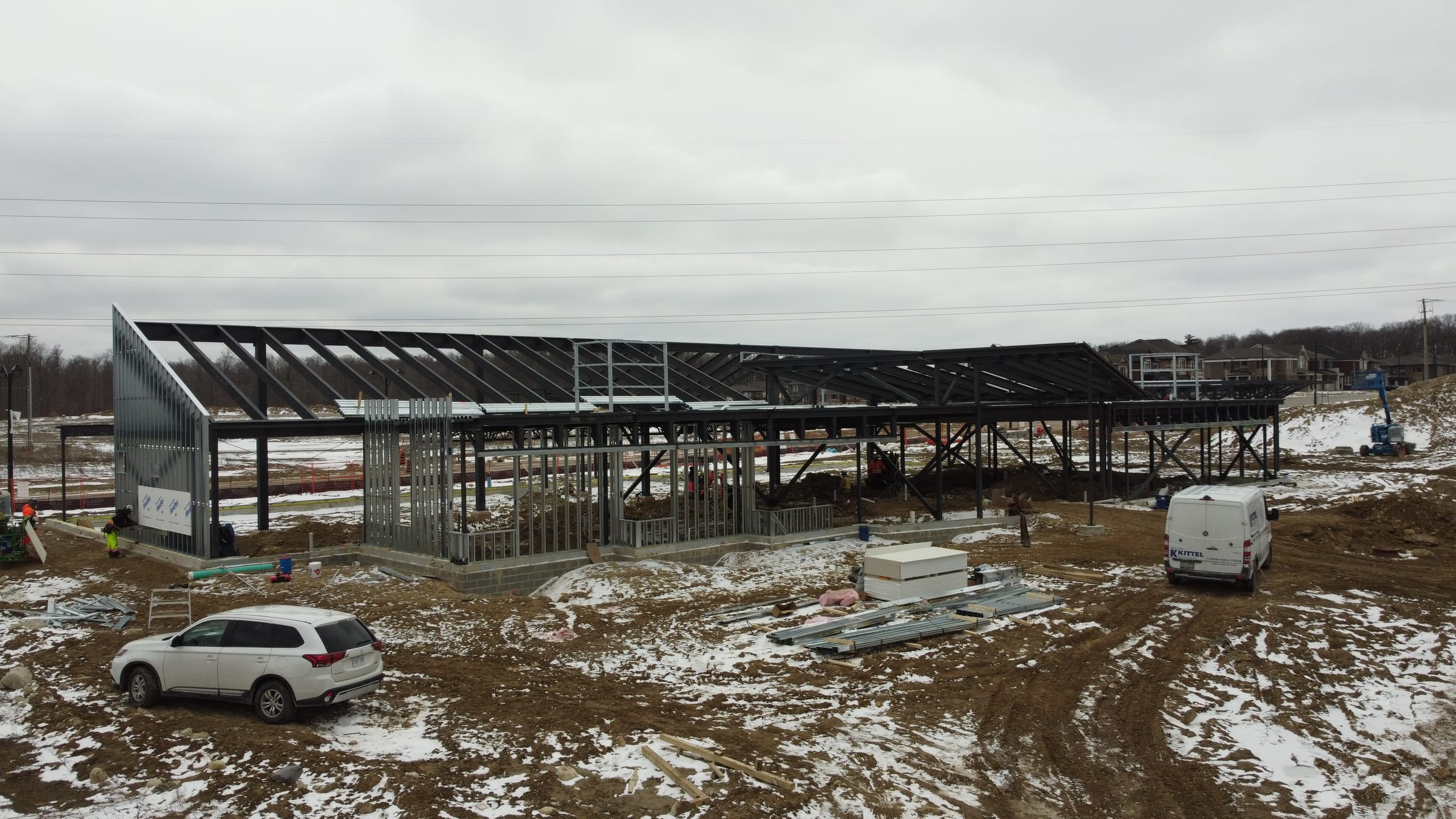 The front of the library's steel frame, with sloped roof members over steel-stud walls and a muddy, snowy site in front.