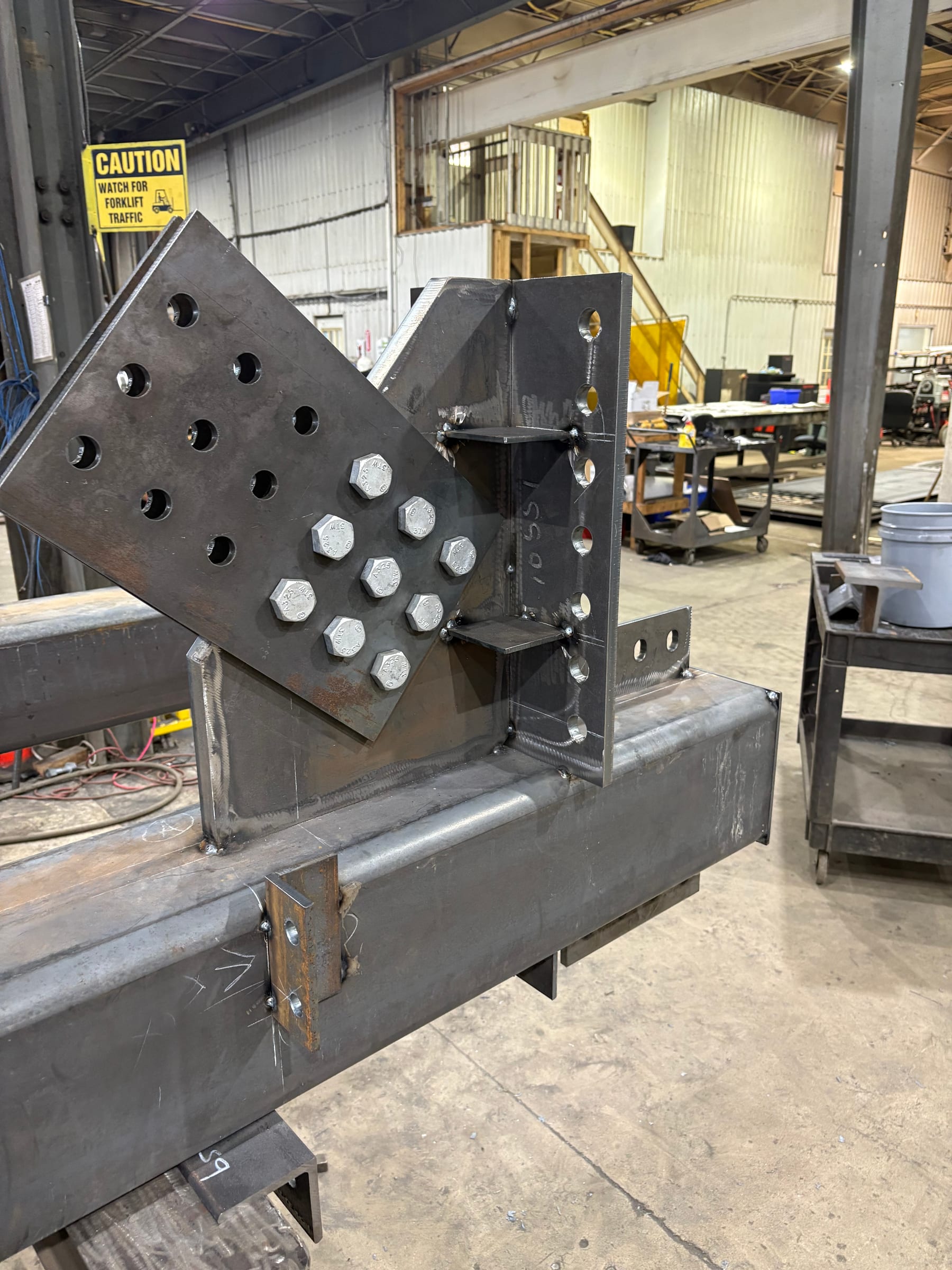 Close-up of a fabricated steel member in the shop: a gusset plate bolted to a connection, with a row of installed bolts.