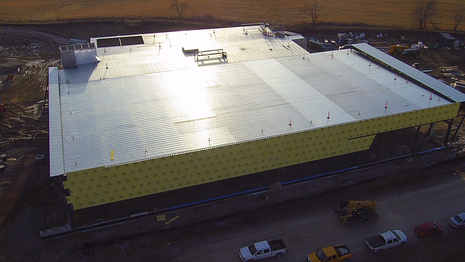 An aerial view of the building with its roof deck on and yellow sheathing on the walls, with pickups parked beside it.